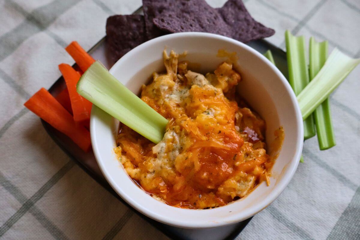 serving dish filled with dairy-free buffalo chicken dip with vegetable sticks and chips