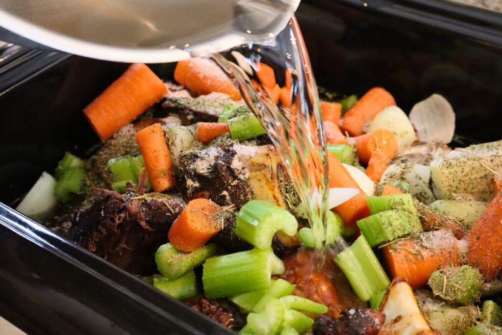 How to Make Beef Bone Broth in an Electric Roaster (Large Batch, From Scratch) 11 Adding water to a roaster with beef bone broth ingredients inside