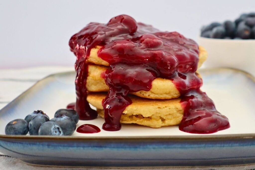 Fluffy almond flour pancakes covered with fruit sauce sitting on a plate with blueberries