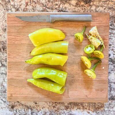 Banana Peppers on cutting board sweet banana peppers with the tops cut off laying on a cutting board with a knife