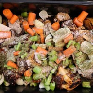 Veggies and herbs Roaster filled with roasted beef bones, chopped veggies, and herbs