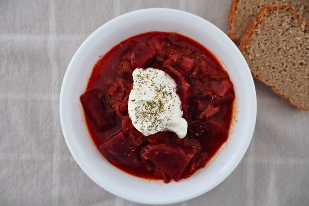 bowl of borscht soup with sour cream on top and slices of bread in the back round