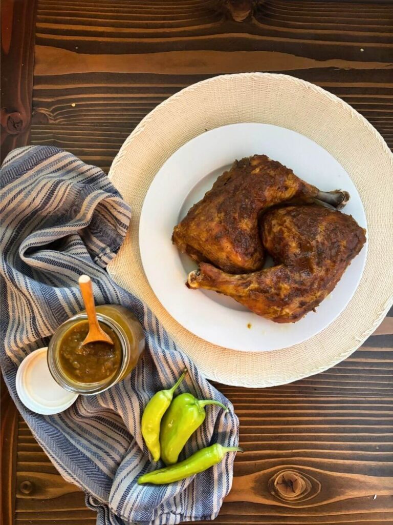 baked chicken covered in banana pepper sauce with a jar full of banana pepper sauce and whole banana peppers on a table