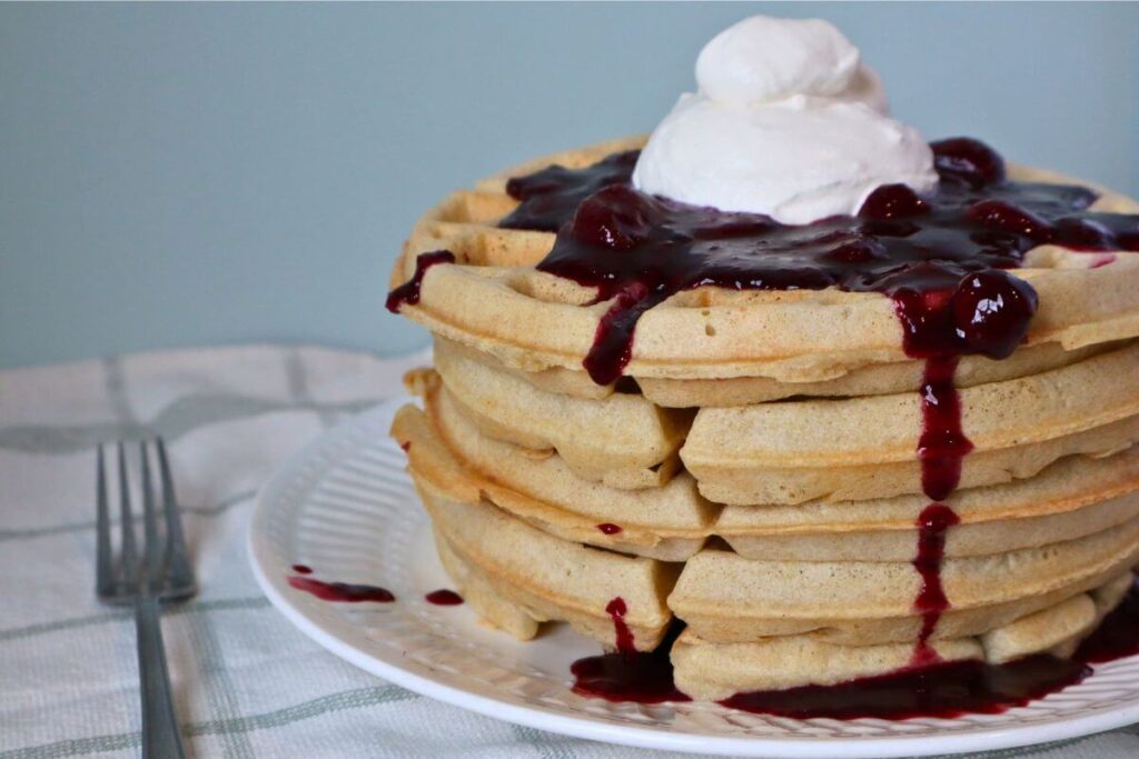 Stack of waffles topped with berry sauce and whipped cream