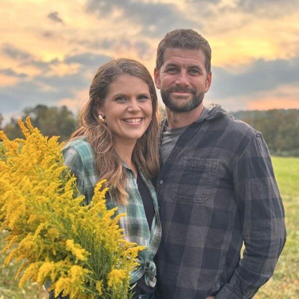 man and woman standing in a field holding golden rod and smiling