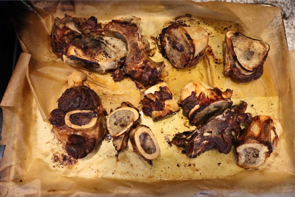 How to Make Beef Bone Broth in an Electric Roaster (Large Batch, From Scratch) 9 beef bones roasting on a sheet pan for large batch bone broth
