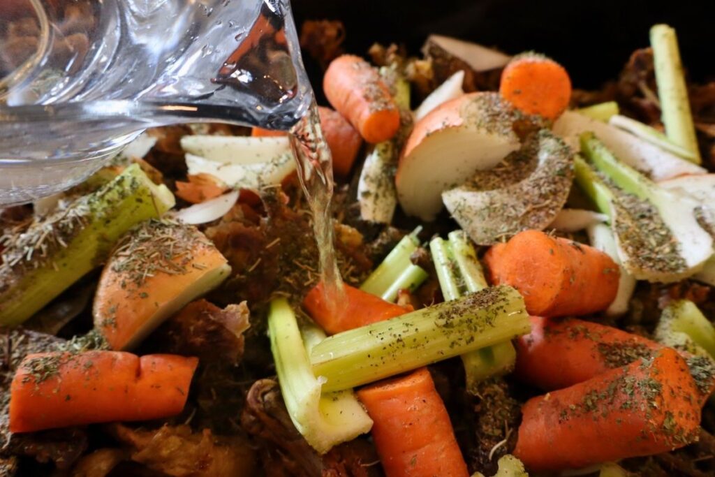 adding water to chicken bone broth ingredients in an electric roaster