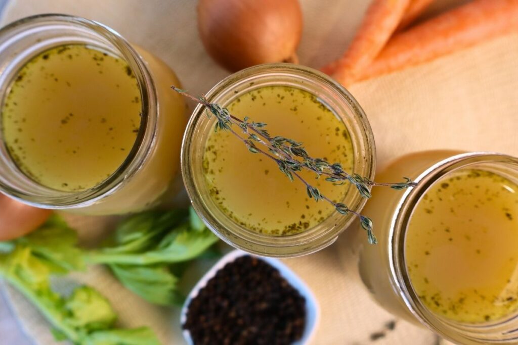 Overhead view of three open mason jars filled with homemade bone broth, vegetables, and peppercorns