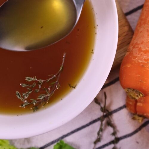 homemade chicken bone broth served in a bowl with herbs and carrots