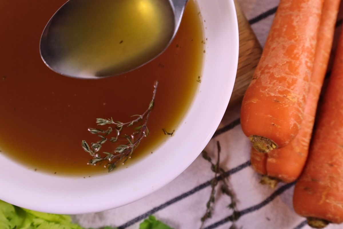 homemade chicken bone broth served in a bowl with herbs and carrots