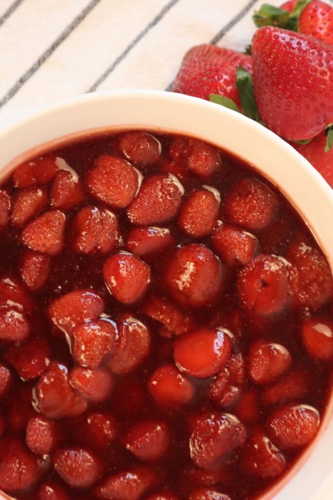 Close-up of chunky strawberry sauce with real strawberry pieces and fresh strawberries on the side.