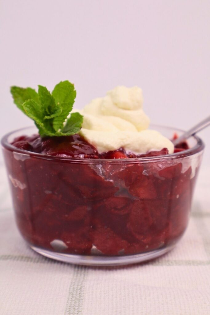 Homemade strawberry sauce served with whipped cream in a clear glass dish, garnished with mint.