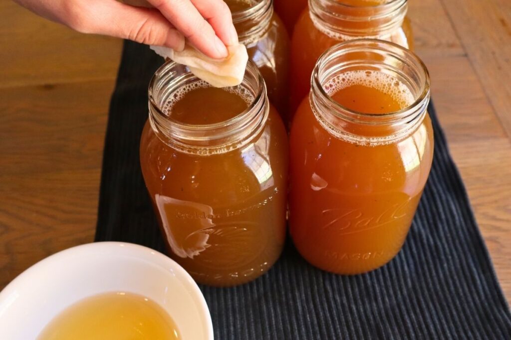 Using a paper towel soaked in vinegar to clean the rim of a jar to prepare them for pressure canning.