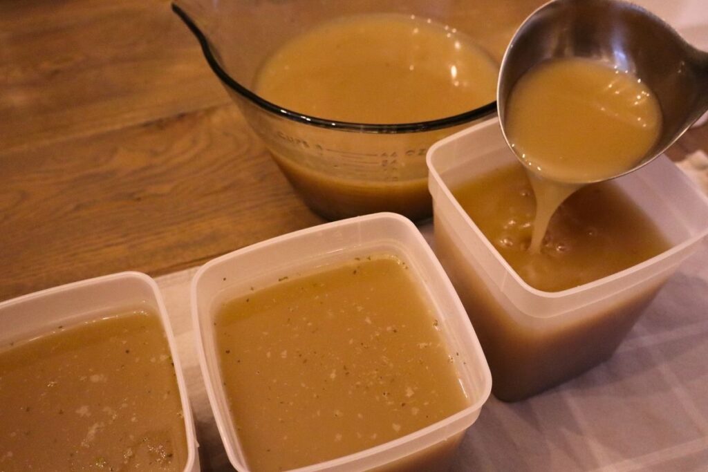 A ladle pouring bone broth into containers to go in the freezer for use in soups, stews, sauces, and recipes.