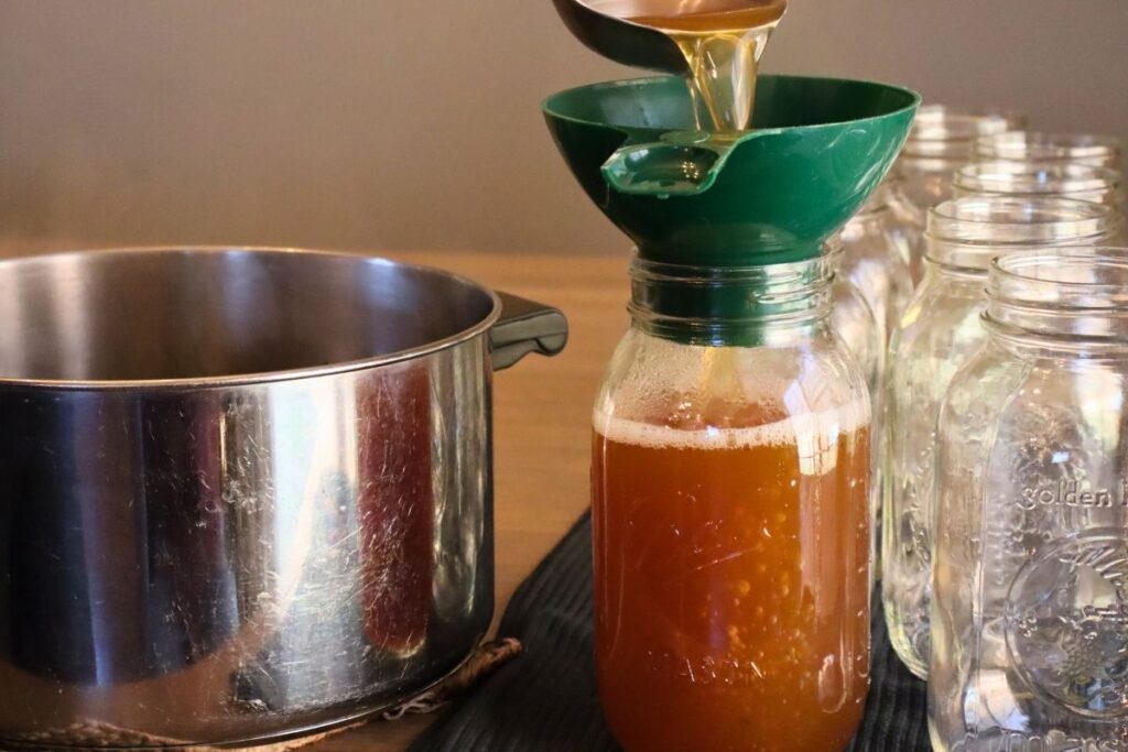 Ladling bone broth into a jar with empty jars ready to be filled for making rich-gelatinous bone broth.