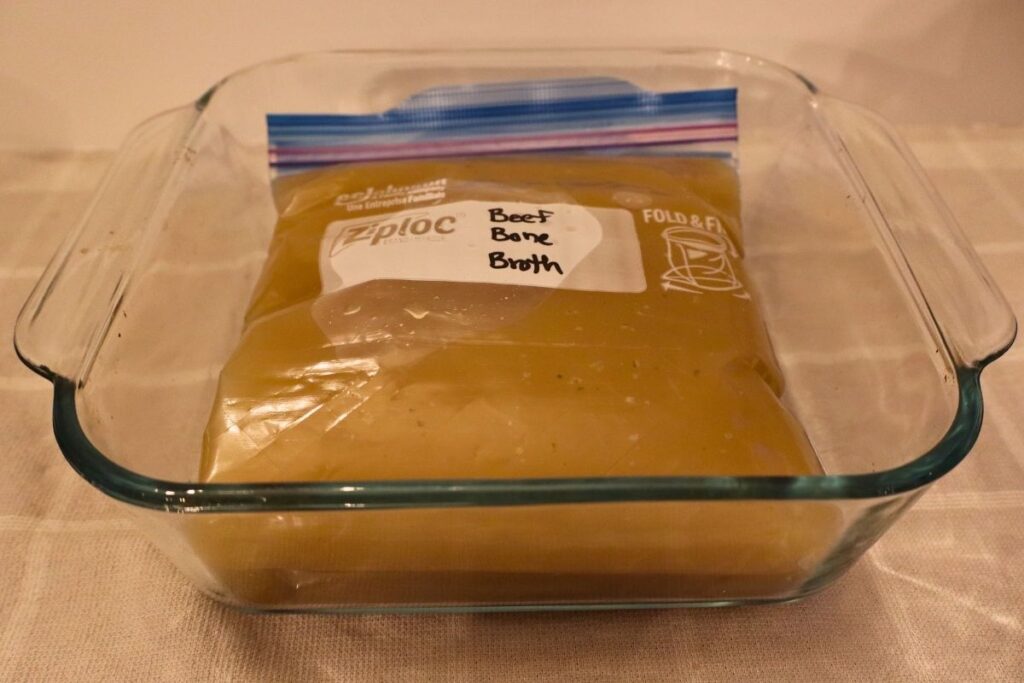 Pyrex casserole dish filled with stacked Ziplock bags of beef bone broth ready to freeze for soups, stews, and from-scratch cooking.
