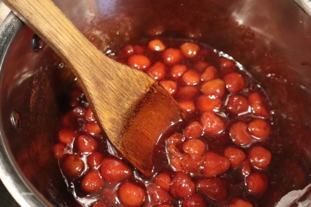 Kettle of glossy homemade strawberry sauce showing smooth texture.