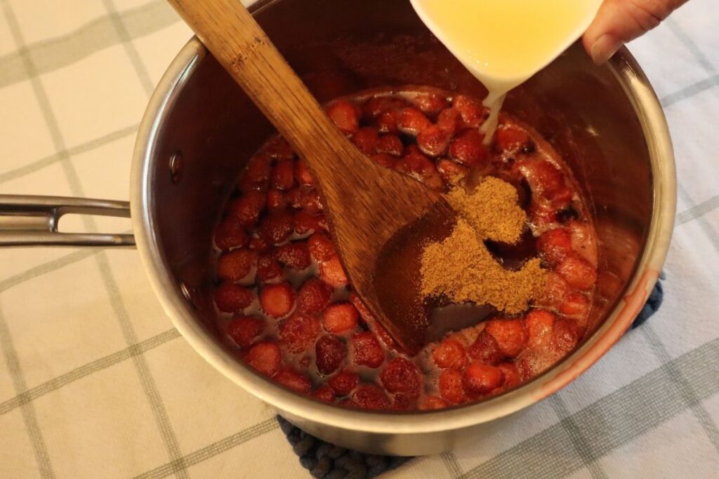 Adding ingredients to a kettle for strawberry sauce.