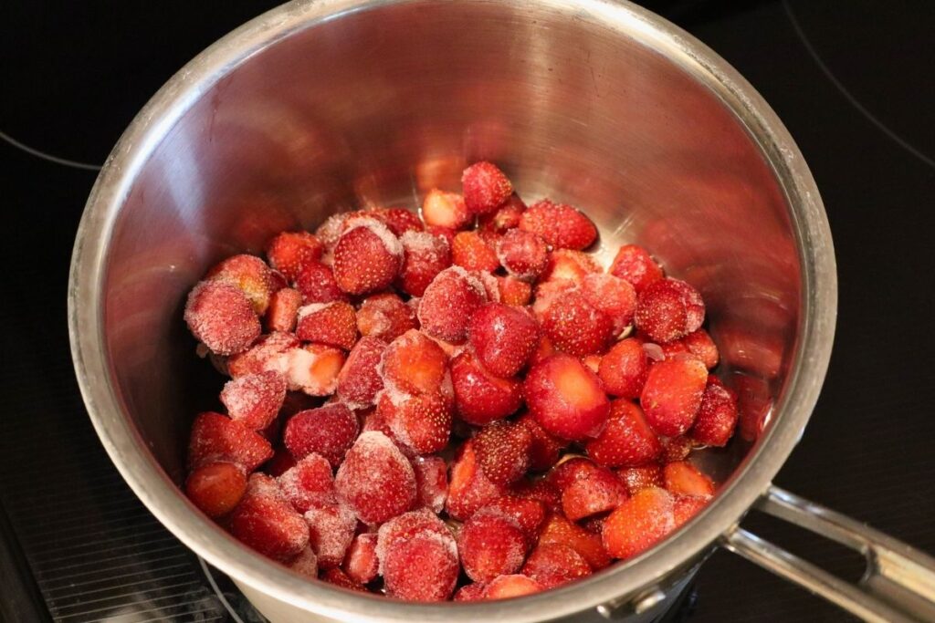 A kettle filled with frozen strawberries before heating.