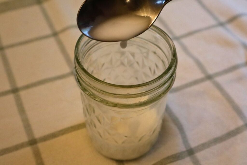 A small cup of arrowroot slurry prepared for thickening strawberry sauce dripping from a spoon.