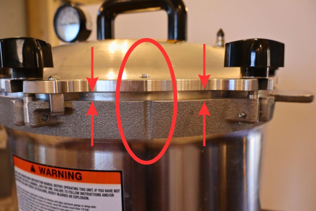 Closeup picture of a pressure canner with the arrow on the lid lined up with the groove in the canner bottom, and showing equal spacing between the canner lid and the canner.