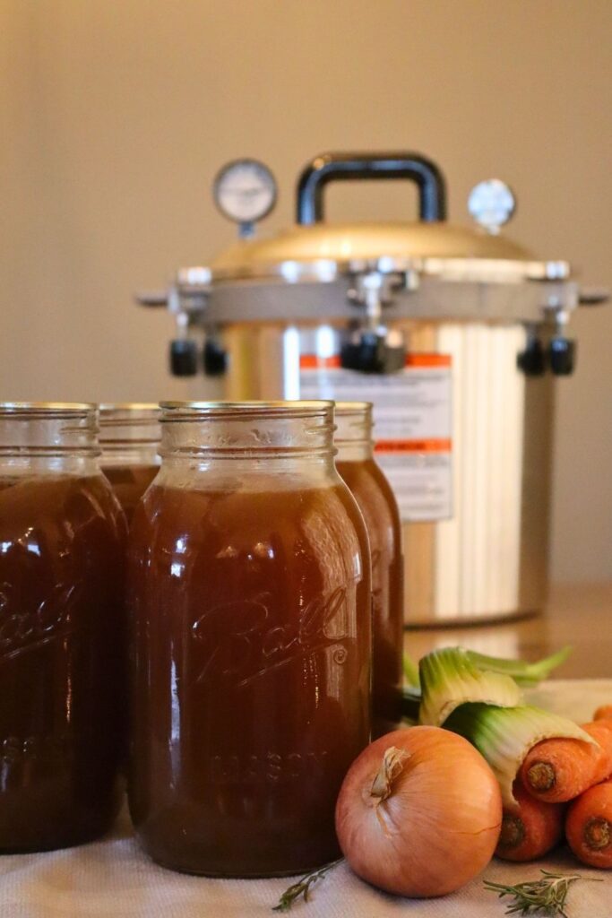 Simple from-scratch bone broth jars with carrots, onion, and celery with a pressure canner in the background.