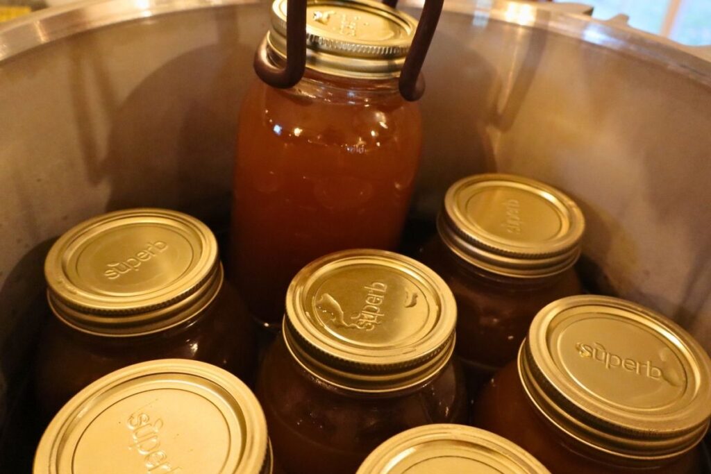 Using a jar lifter to remove hot jars from a pressure canner after processing.