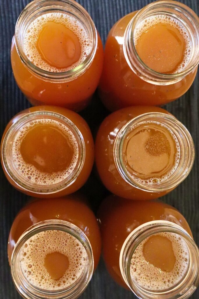 How to pressure can bone broth—six open jars filled with rich golden broth shot from above, prepped and ready for the pressure canner.