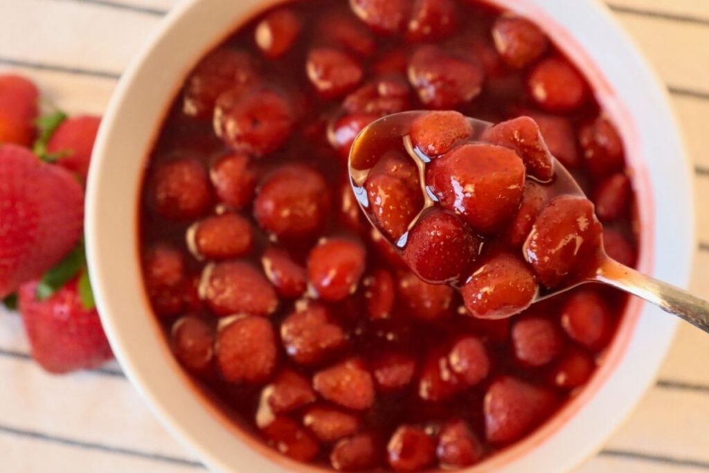 Close-up of strawberry sauce on a spoon over a bowl showing its smooth texture.