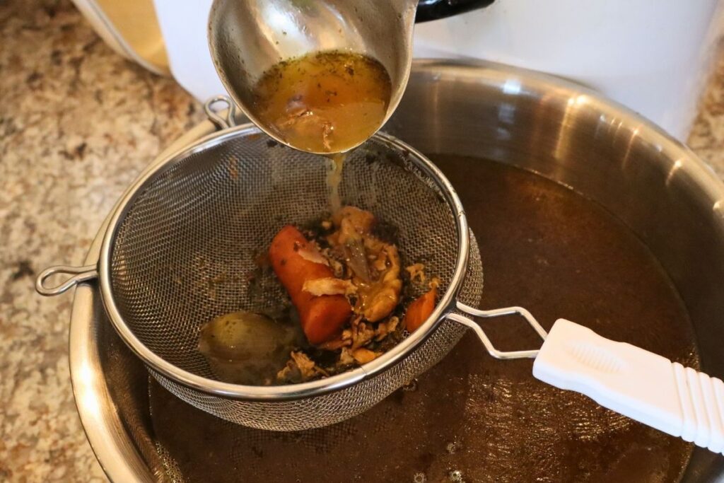 straining chicken bone broth through a fine mesh strainer