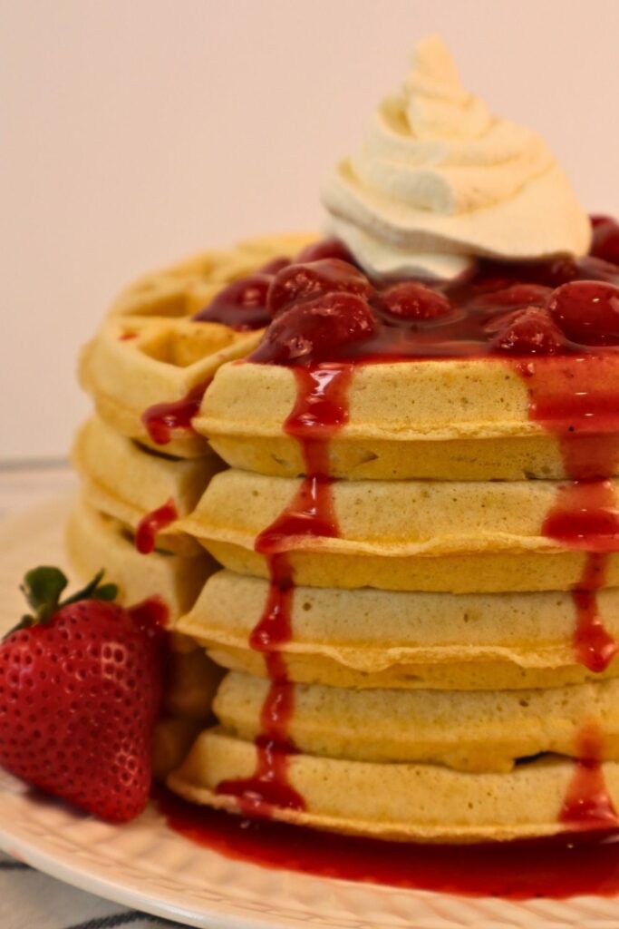 Gluten-free waffles topped with homemade strawberry sauce and whipped cream — easy, frozen strawberry breakfast idea.”