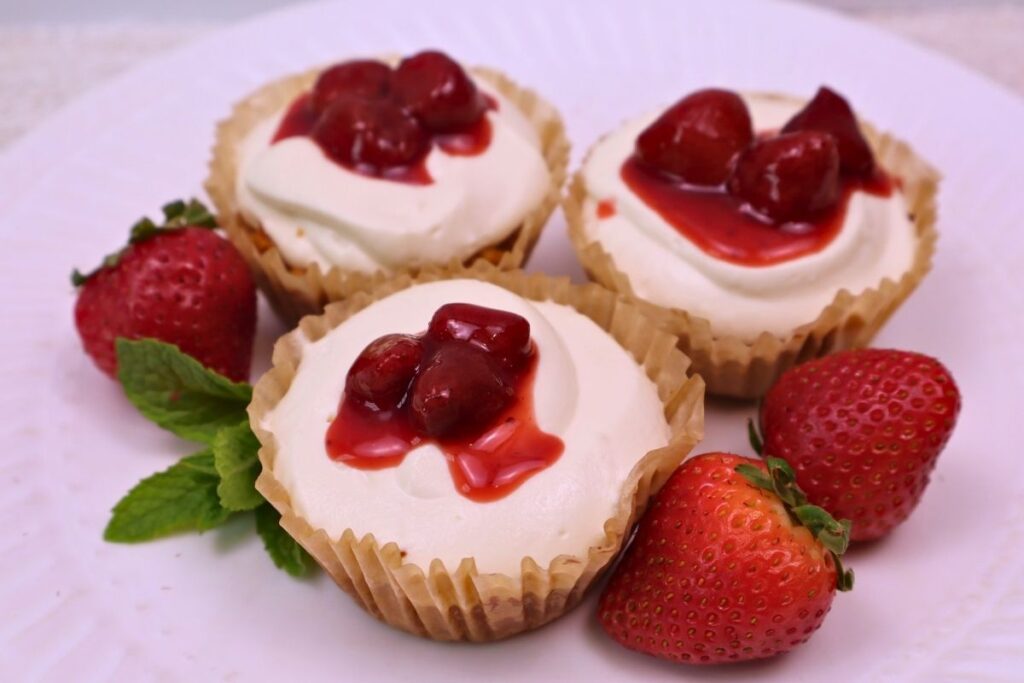 Mini cheesecakes served with fresh strawberry sauce on top.