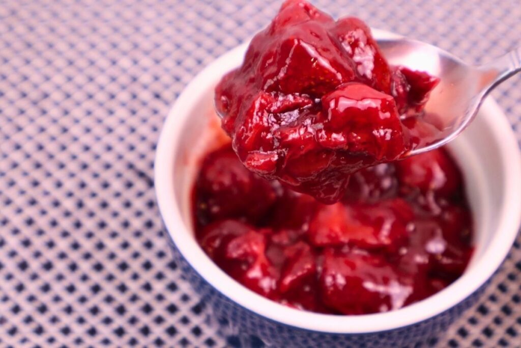 Closeup of thick homemade strawberry sauce resting on a spoon to show its texture.
