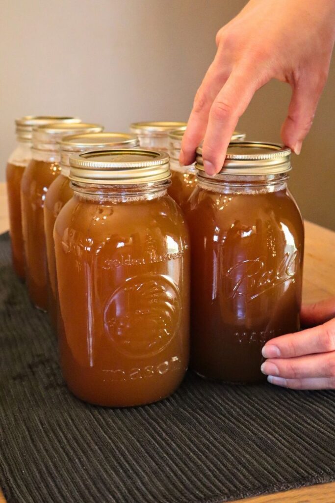 Using three fingers to tighten a canning ring on a mason jar of bone broth.