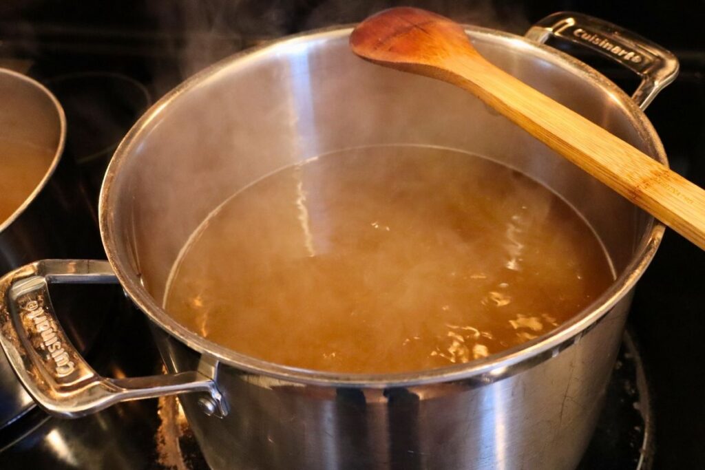 Stockpot filled with steaming hot bone broth on the stove with a wooden spoon.