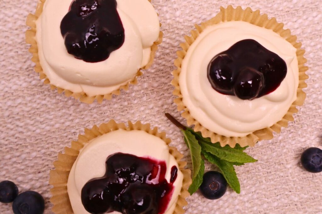 3 mini cheesecakes on a white background topped with thick blueberry sauce.