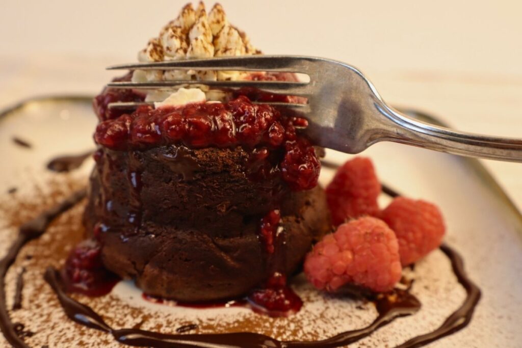 How to Make Raspberry Sauce with Frozen Raspberries 15 Fork cutting into a chocolate lava cake topped with raspberry sauce.