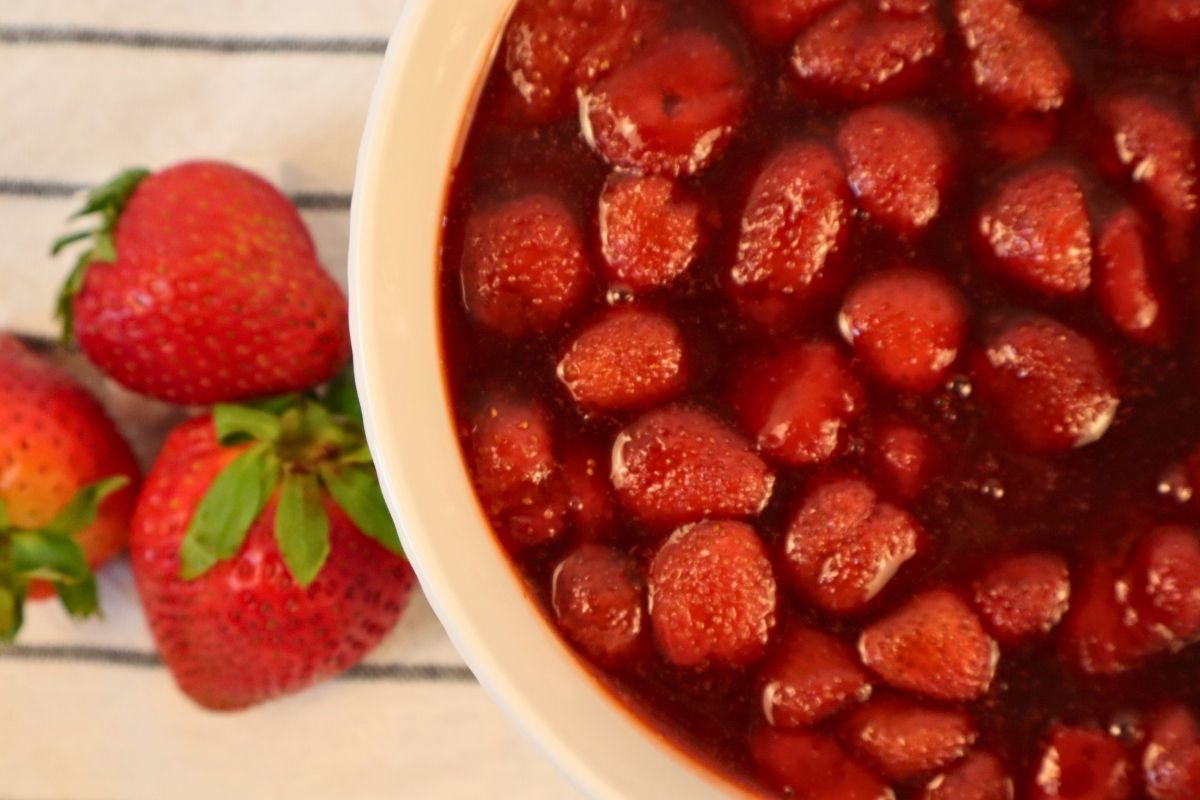 Overhead view of a bowl of homemade chunky strawberry berry sauce surrounded by fresh strawberries