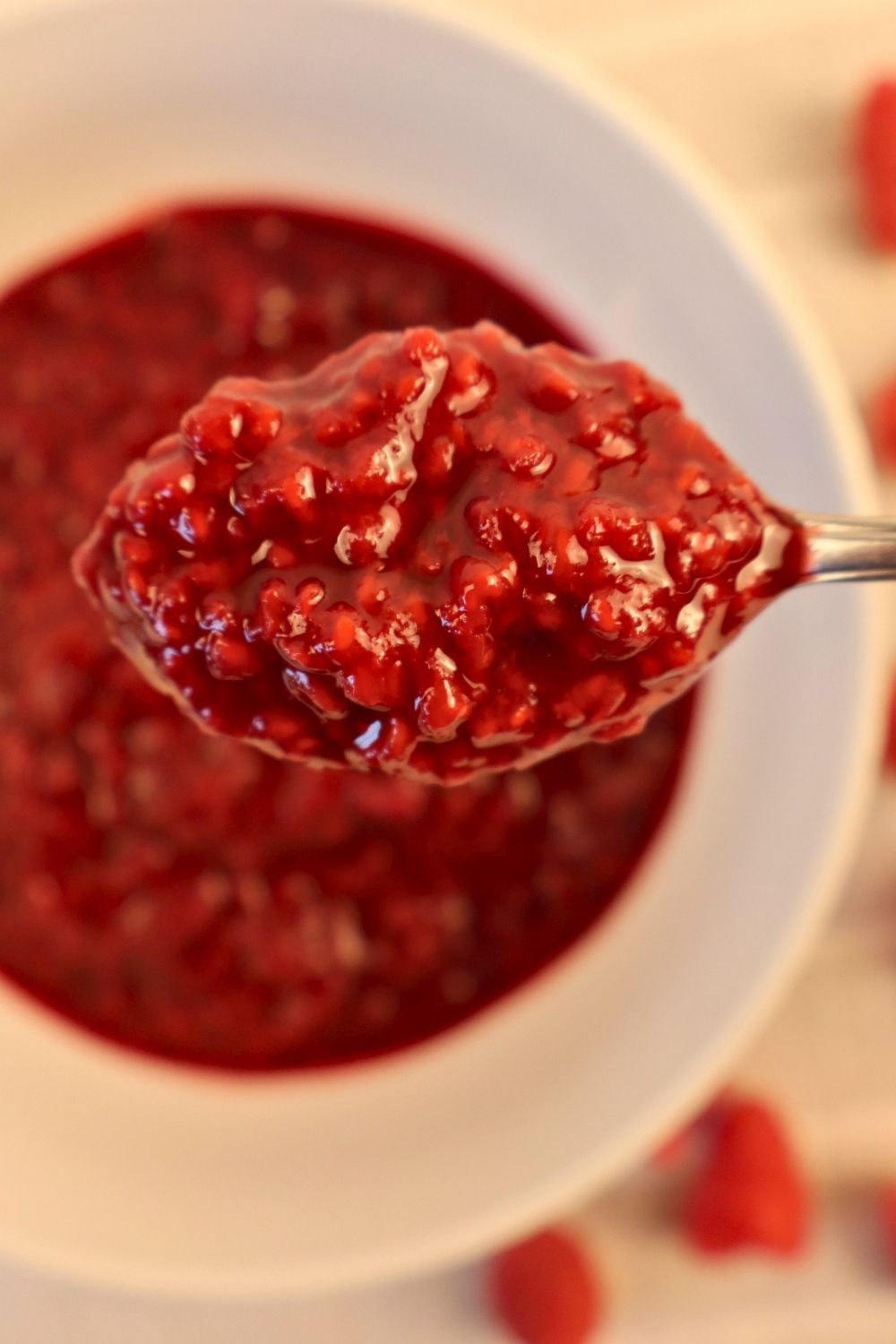 How to Make Raspberry Sauce with Frozen Raspberries 9 Spoonful of homemade raspberry sauce held over a bowl — easy berry sauce recipe for desserts.