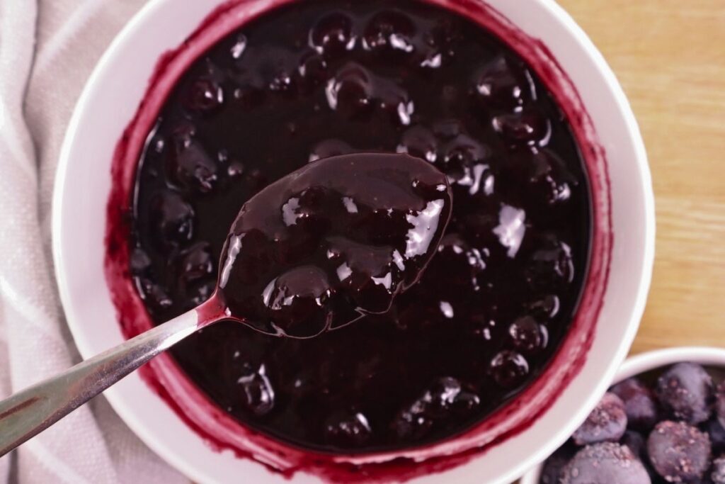 A spoonful of blueberry sauce held above a bowl full of blueberry sauce