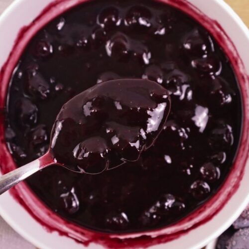 A spoonful of blueberry sauce held above a bowl full of blueberry sauce