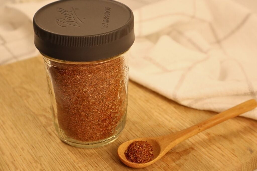 A jar of homemade taco seasoning with a wooden spoon lying beside it
