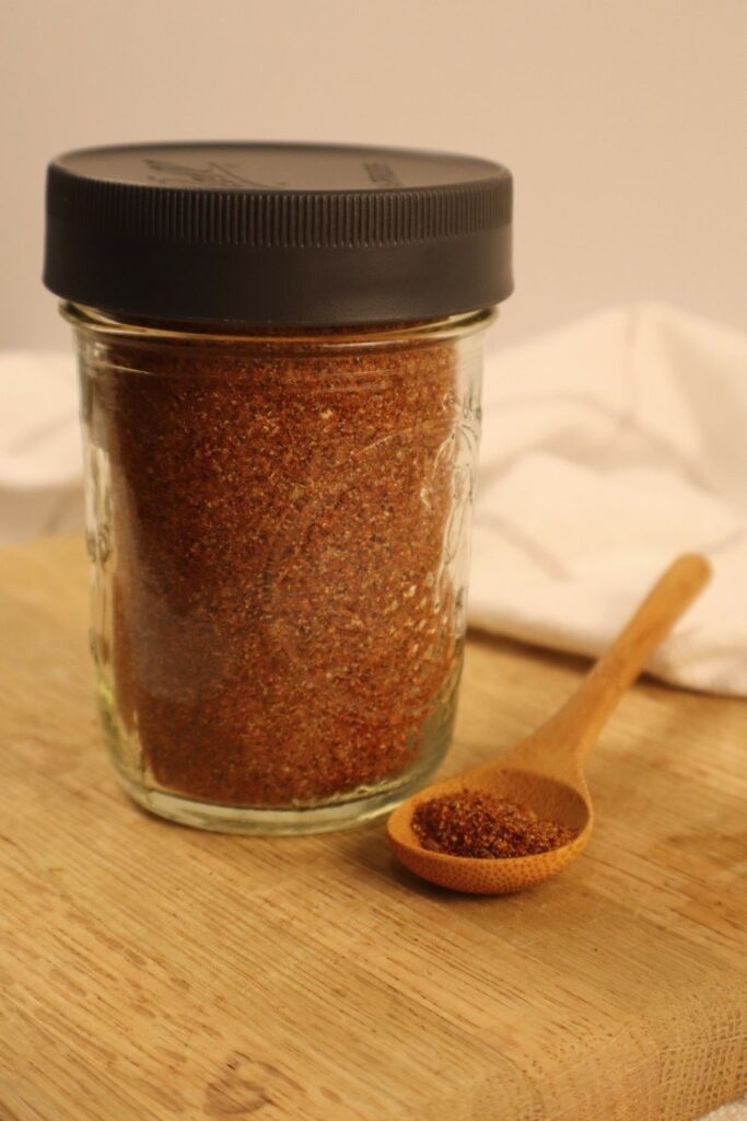 Jar filled with homemade taco seasoning with a spoon beside it — easy DIY taco seasoning recipe.