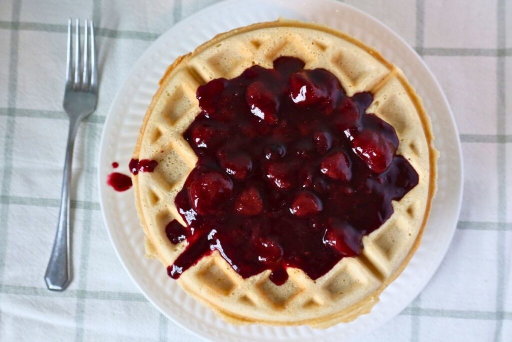 Overhead shot of homemade mixed berry sauce poured over waffles with a fork alongside