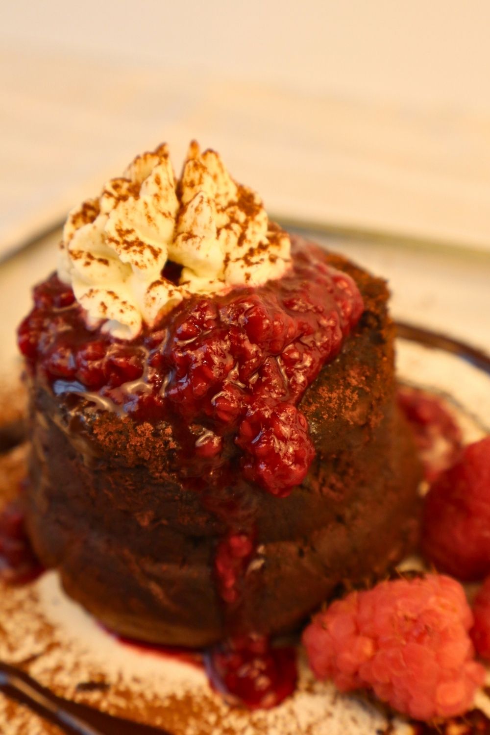 Close-up of rich chocolate lava cake drizzled with homemade raspberry sauce, fresh raspberries, and whipped cream — decadent berry sauce dessert idea