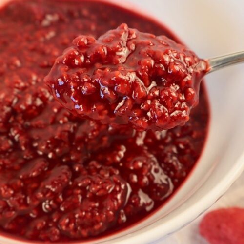 How to Make Raspberry Sauce with Frozen Raspberries 16 Close-up of a spoonful of raspberry sauce with a bowl of sauce in the background.
