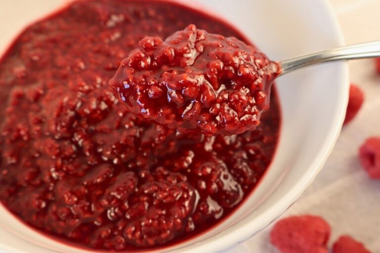 Close-up of a spoonful of raspberry sauce with a bowl of sauce in the background.