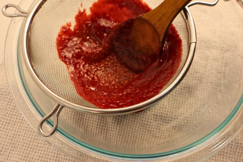 How to Make Raspberry Sauce with Frozen Raspberries 12 Straining raspberry sauce through a fine-mesh strainer with a spoon to remove the seeds.