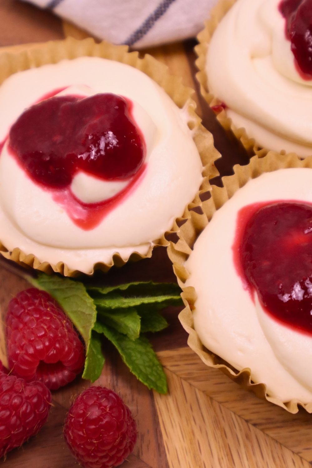 Overhead shot of mini cheesecakes drizzled with smooth homemade seedless raspberry sauce and fresh raspberries — easy berry sauce recipe for elegant desserts