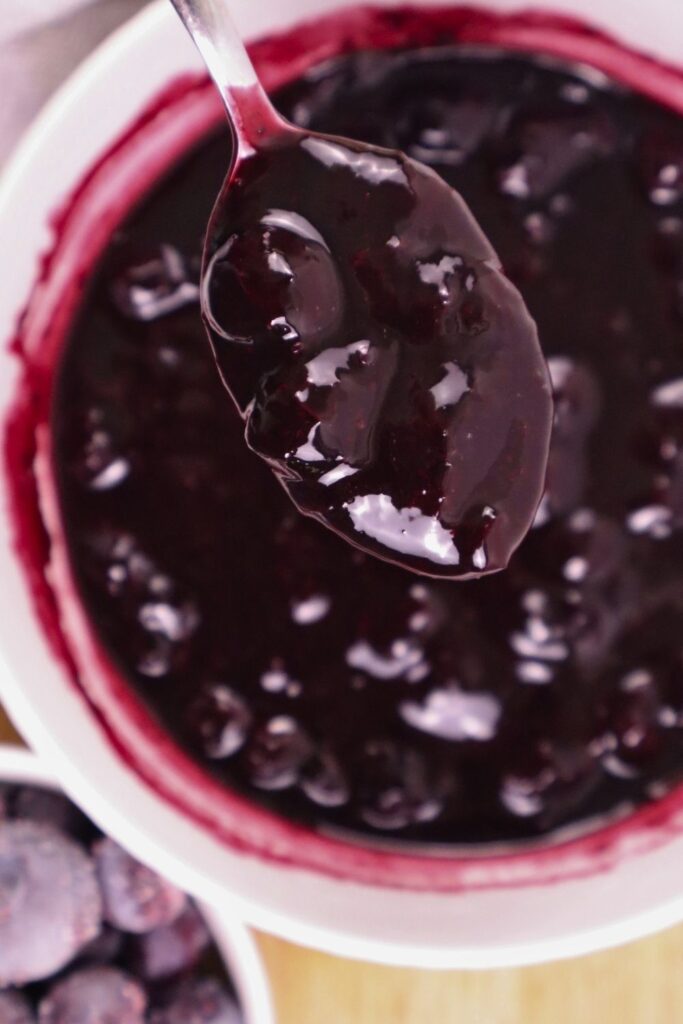 A spoonful of thick blueberry sauce held above a bowl of sauce.